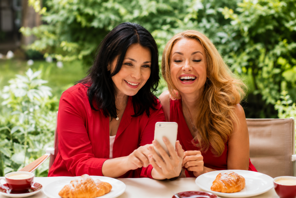 Two midlife women in red outfits smiling while looking at a smartphone together during a conversation about gut health and hormones.