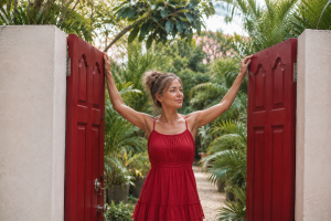Confident midlife woman in a red dress standing at an open garden gate, representing hope and healing from recurrent BV.