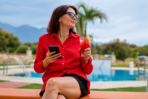Midlife woman in a red blouse relaxing by a pool with a refreshing drink, representing healthy lifestyle habits that support balanced cortisol levels.